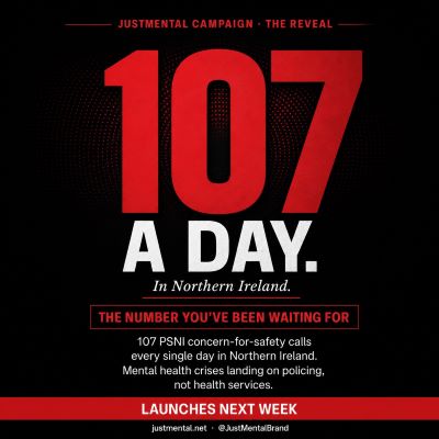 107 a day campaign reveal graphic from JustMental News. Black tile with red strips top and bottom. Eyebrow text reads: “JustMental Campaign · The Reveal.” Massive red display: 107, set against a subtle halftone dot pattern that radiates outward. Below in white: “A DAY.” Italic line: “In Northern Ireland.” Red outlined box containing the kicker: “The number you’ve been waiting for.” Body text: 107 PSNI concern-for-safety calls every single day in Northern Ireland. Mental health crises landing on policing, not health services. Red footer strip: “Launches next week.”